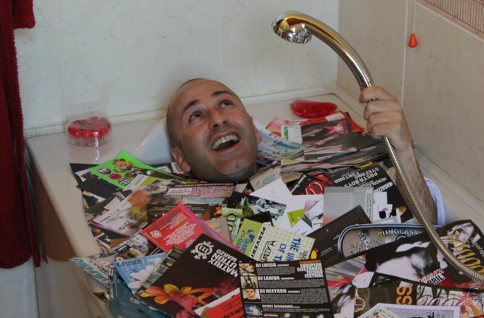 Marco Brusadelli lying in a bathtub filled with flyers from his rave flyer collection